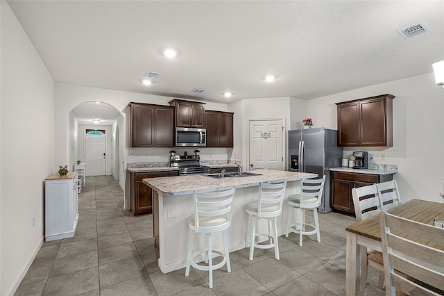 kitchen featuring sink, a breakfast bar, appliances with stainless steel finishes, dark brown cabinets, and an island with sink