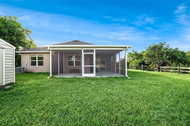 rear view of house featuring central air condition unit, a patio area, a sunroom, and a lawn