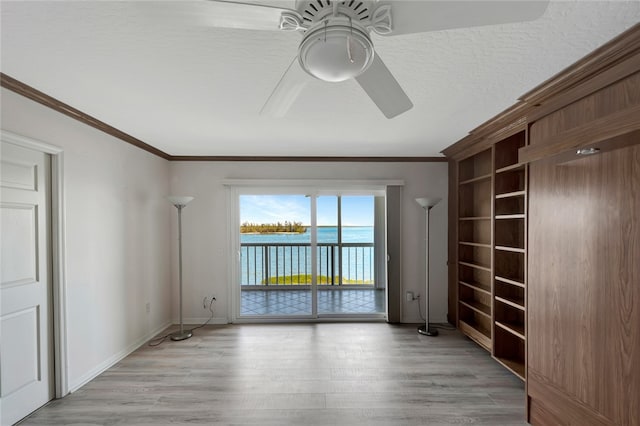 spare room featuring ornamental molding, a textured ceiling, a water view, ceiling fan, and light hardwood / wood-style flooring