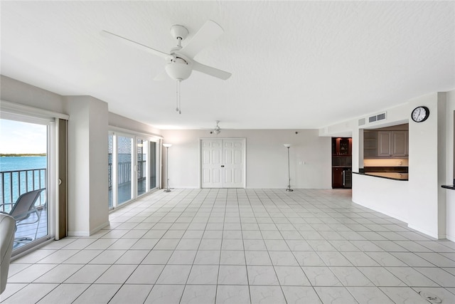 unfurnished living room featuring ceiling fan, a textured ceiling, light tile patterned floors, and a water view