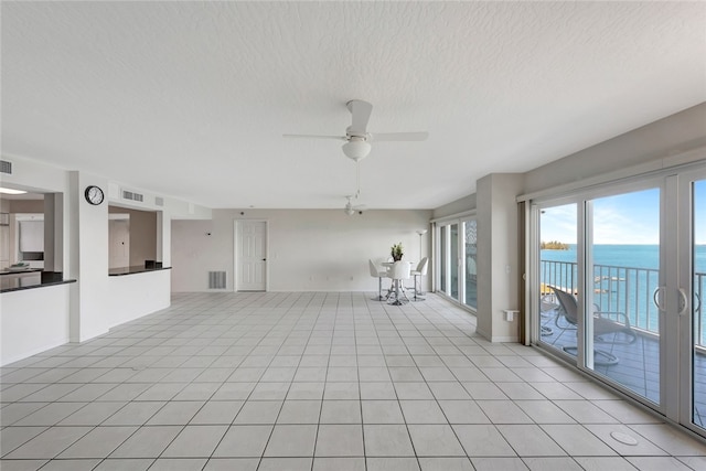 unfurnished living room featuring a water view, a textured ceiling, light tile patterned floors, and ceiling fan