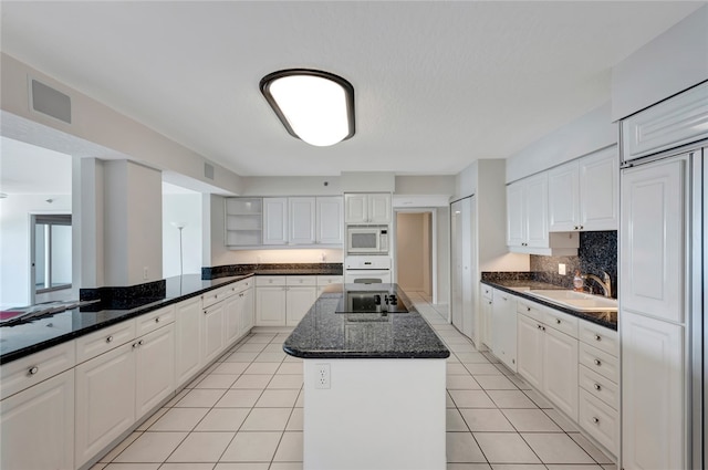 kitchen with built in appliances, white cabinetry, sink, dark stone counters, and a center island