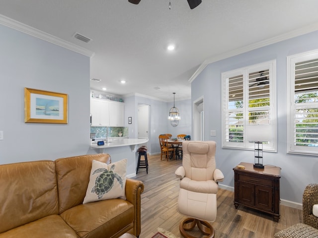 living room featuring ceiling fan with notable chandelier, light hardwood / wood-style flooring, and crown molding