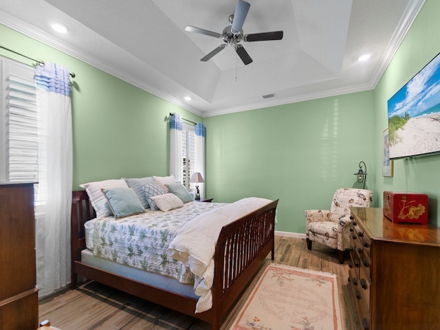 bedroom with hardwood / wood-style floors, ceiling fan, crown molding, and a tray ceiling