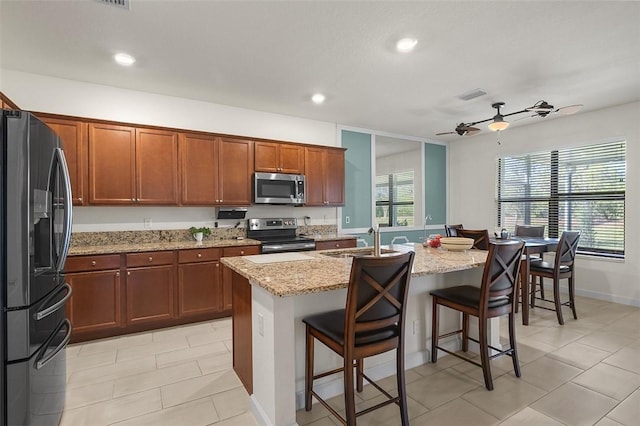 kitchen featuring sink, a kitchen breakfast bar, a kitchen island with sink, stainless steel appliances, and light stone countertops