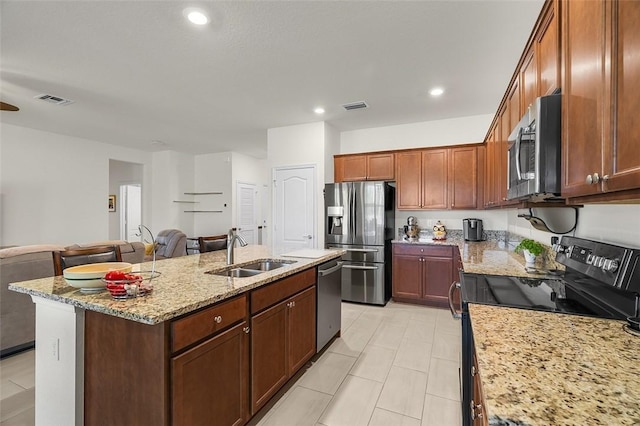 kitchen featuring a kitchen island with sink, sink, light stone countertops, and appliances with stainless steel finishes