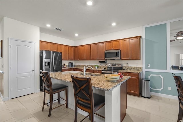 kitchen featuring light stone counters, appliances with stainless steel finishes, an island with sink, and a breakfast bar area