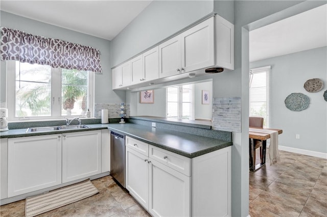 kitchen with stainless steel dishwasher, dark countertops, a sink, and white cabinetry