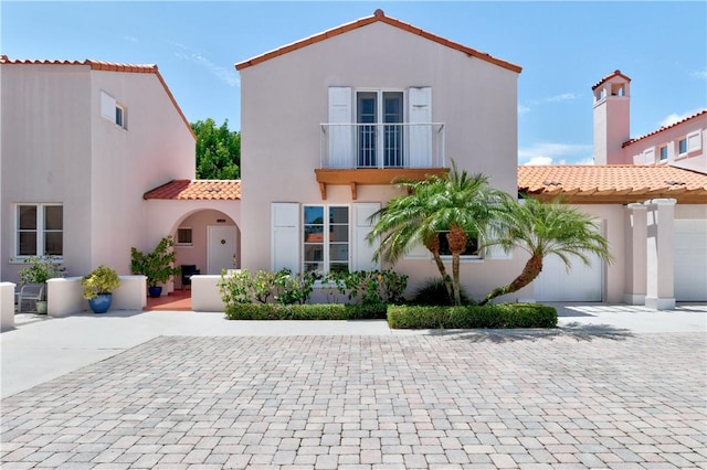 mediterranean / spanish home featuring decorative driveway, stucco siding, a balcony, a garage, and a tiled roof