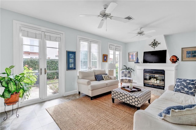 living room featuring light tile patterned floors, ceiling fan, visible vents, baseboards, and a glass covered fireplace