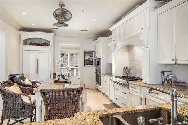 kitchen featuring built in appliances, white cabinetry, sink, and light stone counters