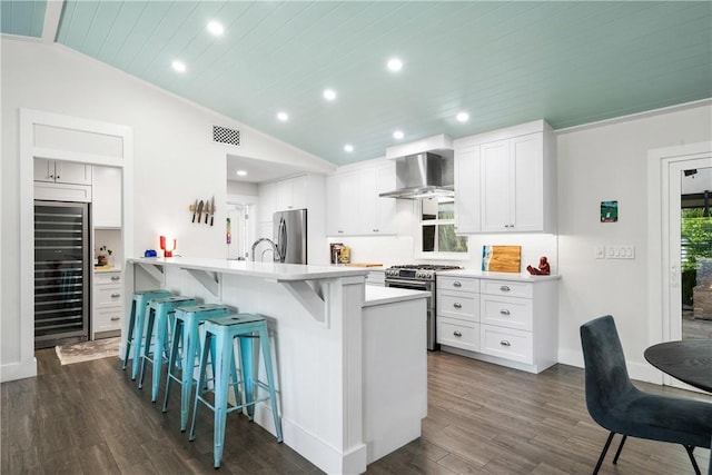 kitchen featuring beverage cooler, visible vents, vaulted ceiling, appliances with stainless steel finishes, and wall chimney exhaust hood