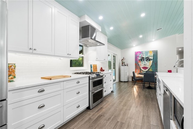 kitchen with white cabinets, appliances with stainless steel finishes, light wood-type flooring, wall chimney exhaust hood, and tasteful backsplash