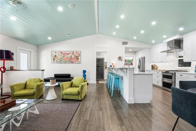 kitchen featuring wooden ceiling, wall chimney range hood, a breakfast bar area, white cabinetry, and stainless steel appliances