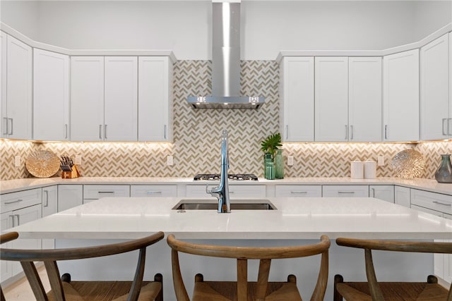 kitchen featuring tasteful backsplash, white cabinetry, wall chimney exhaust hood, and a breakfast bar area