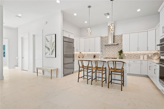 kitchen featuring white cabinets, an island with sink, wall chimney exhaust hood, and stainless steel appliances