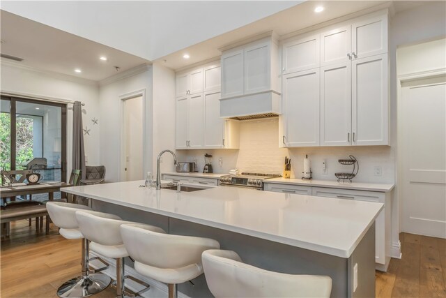 kitchen with white cabinets, light hardwood / wood-style floors, an island with sink, and stainless steel range oven