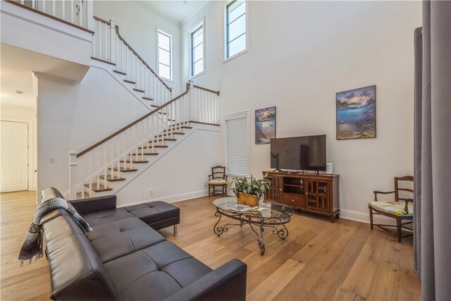 living room featuring crown molding, light wood-type flooring, and a high ceiling