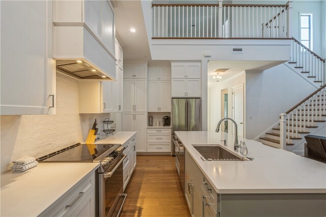 kitchen with appliances with stainless steel finishes, a center island with sink, sink, and dark hardwood / wood-style flooring