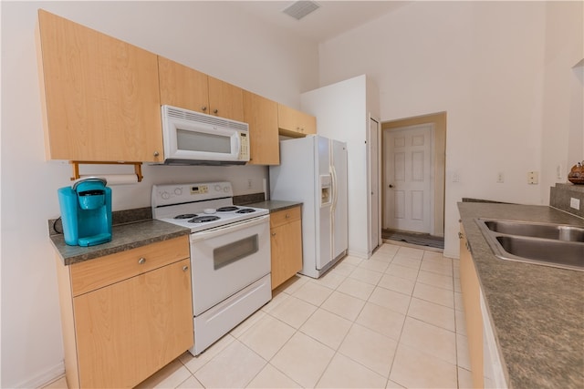 kitchen featuring a towering ceiling, light tile patterned floors, sink, light brown cabinetry, and white appliances