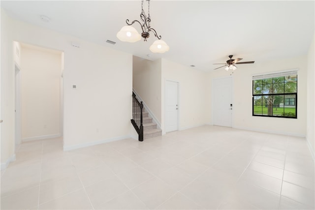 tiled empty room with ceiling fan with notable chandelier