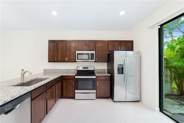 kitchen featuring stainless steel appliances, kitchen peninsula, dark brown cabinetry, sink, and light stone countertops