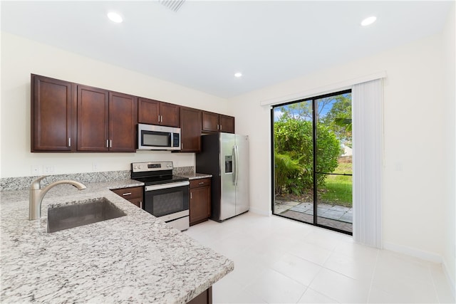 kitchen featuring stainless steel appliances, dark brown cabinetry, light tile patterned floors, sink, and light stone countertops