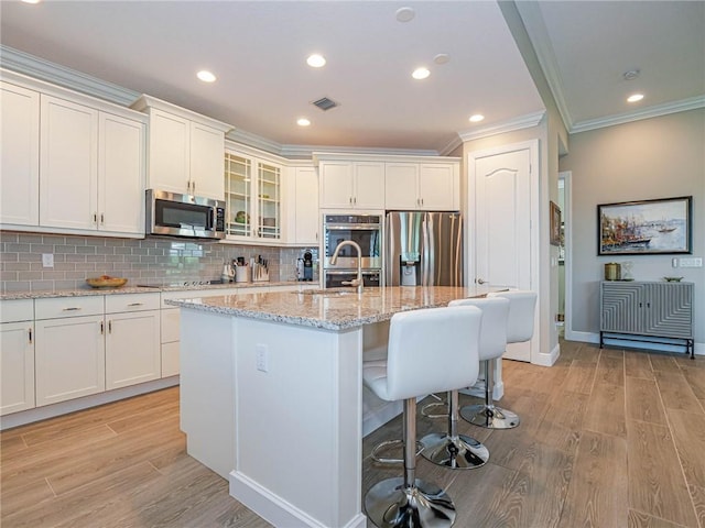 4836 Four Lakes Cir SW, Vero Beach, FL 32968 - kitchen featuring appliances with stainless steel finishes, crown molding, light wood-style floors, a kitchen breakfast bar, and glass insert cabinets