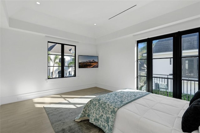 bedroom with a tray ceiling, wood-type flooring, and access to outside