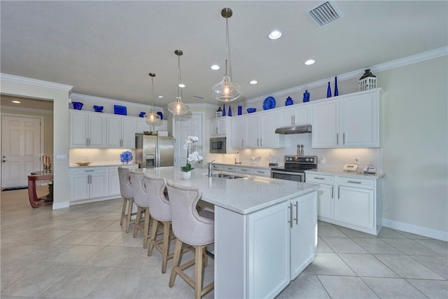 kitchen with pendant lighting, stainless steel appliances, tasteful backsplash, an island with sink, and white cabinets