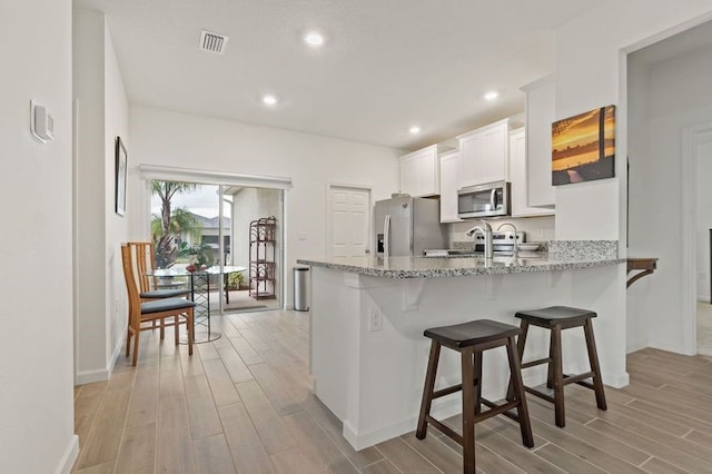 kitchen with stainless steel appliances, light hardwood / wood-style floors, white cabinetry, light stone counters, and kitchen peninsula