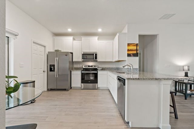 kitchen featuring white cabinetry, kitchen peninsula, light stone counters, a kitchen breakfast bar, and appliances with stainless steel finishes