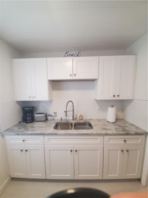 kitchen featuring light stone counters, sink, tasteful backsplash, and white cabinets