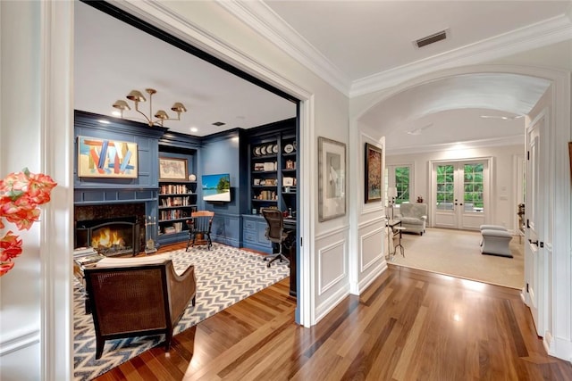 interior space with built in desk, ornamental molding, built in features, a high end fireplace, and hardwood / wood-style floors