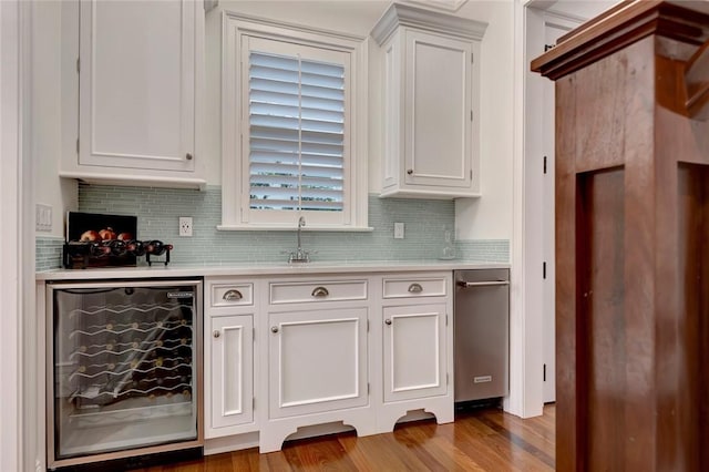 bar with white cabinetry, sink, beverage cooler, backsplash, and light hardwood / wood-style flooring