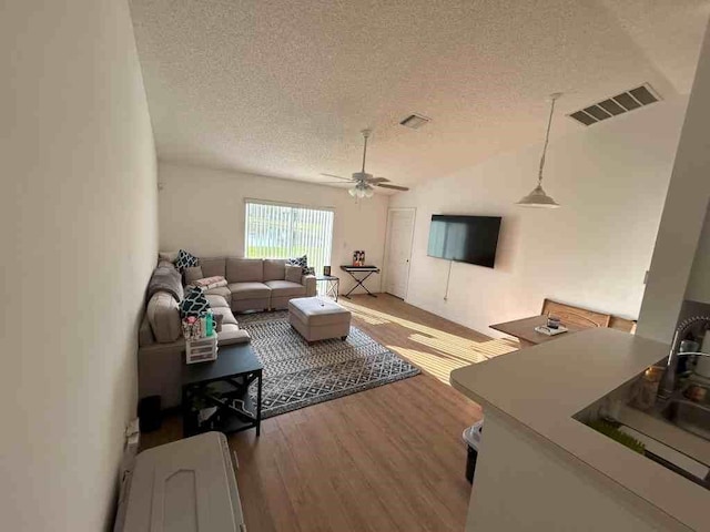 living room with visible vents, a ceiling fan, vaulted ceiling, a textured ceiling, and wood finished floors