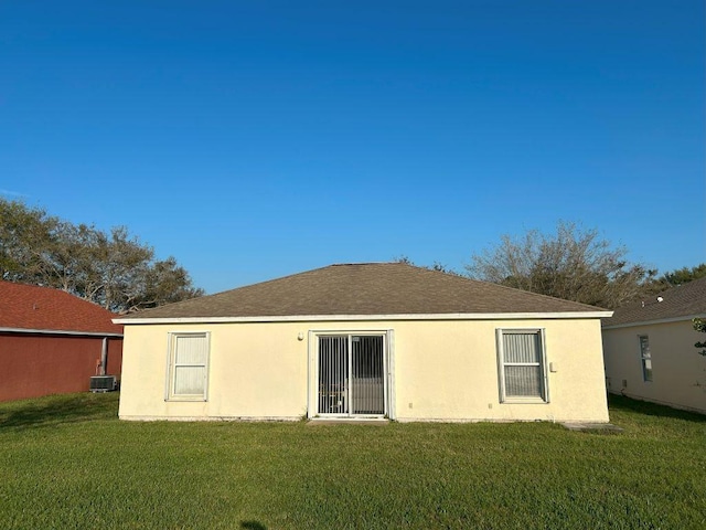 back of house with cooling unit, roof with shingles, a lawn, and stucco siding