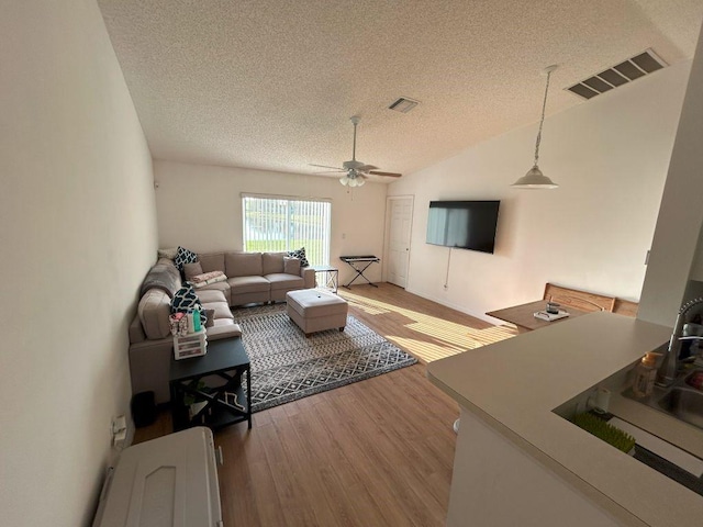 living room featuring a textured ceiling, visible vents, vaulted ceiling, and wood finished floors