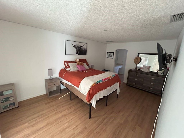 bedroom with light wood-style floors, arched walkways, visible vents, and a textured ceiling