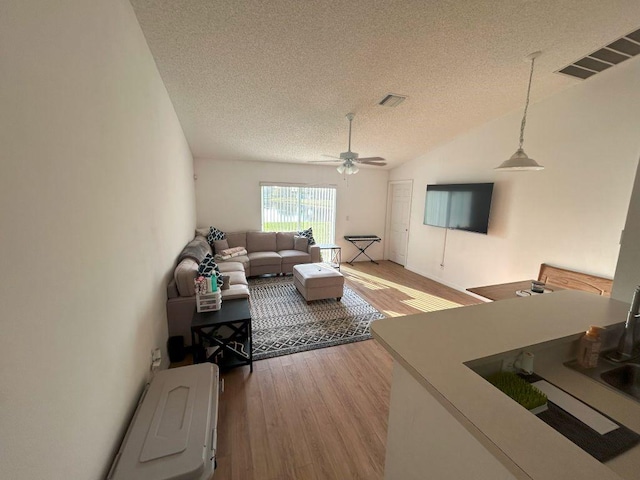 living area with lofted ceiling, visible vents, a textured ceiling, and light wood-style flooring