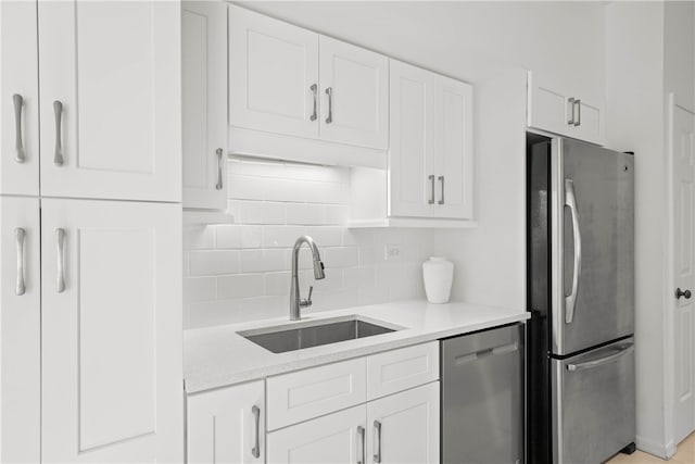 kitchen with light stone countertops, appliances with stainless steel finishes, backsplash, sink, and white cabinetry