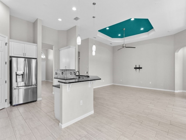 kitchen with white cabinetry, stainless steel refrigerator with ice dispenser, a kitchen bar, a raised ceiling, and pendant lighting