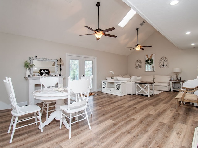 dining area featuring ceiling fan, french doors, light hardwood / wood-style floors, and vaulted ceiling with skylight