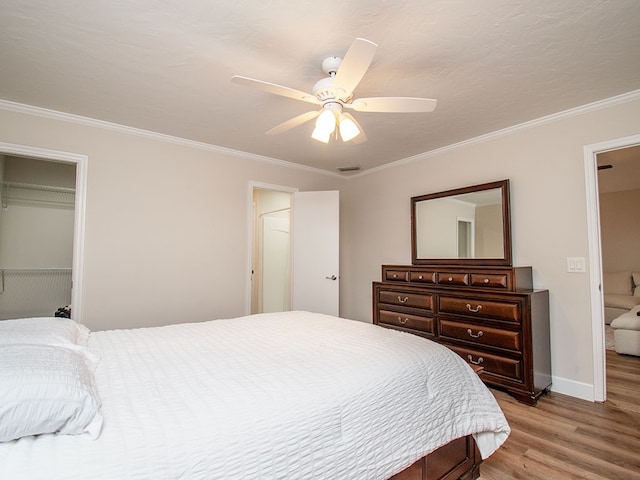 bedroom featuring light hardwood / wood-style flooring, ceiling fan, ornamental molding, connected bathroom, and a closet