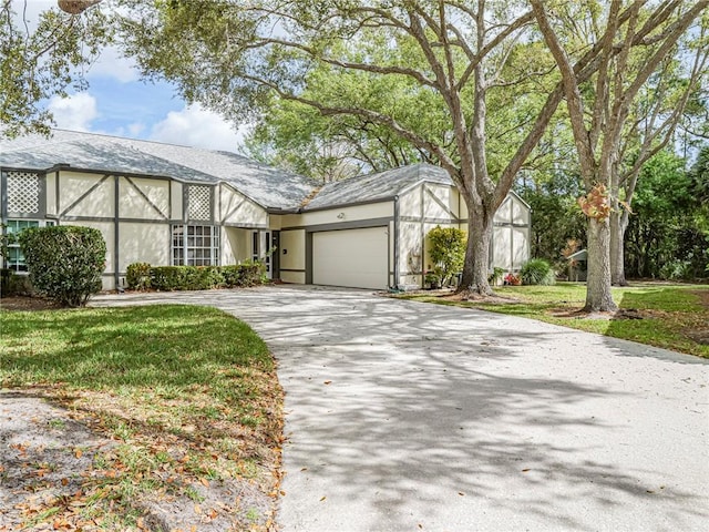 tudor home featuring driveway, a front yard, an attached garage, and stucco siding