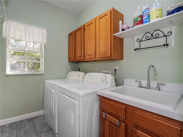 clothes washing area with a sink, washing machine and clothes dryer, cabinet space, and baseboards