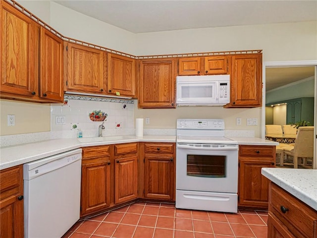 kitchen featuring brown cabinetry, white appliances, light tile patterned flooring, and a sink