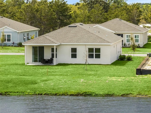 rear view of house with a water view, stucco siding, roof with shingles, and a yard