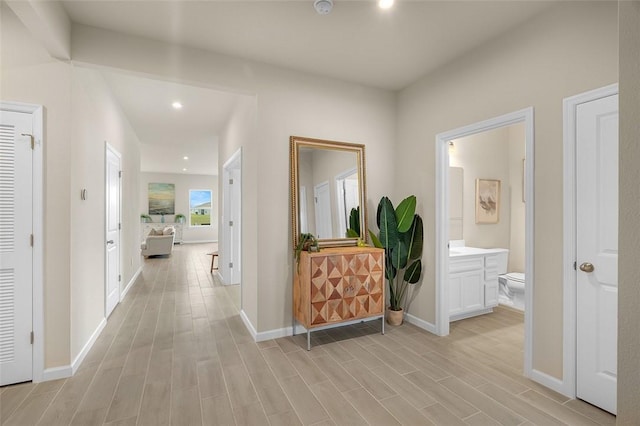 hallway with baseboards, light wood finished floors, and recessed lighting