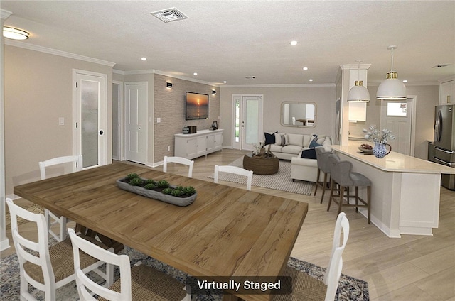 dining area featuring light wood-type flooring, a textured ceiling, and crown molding